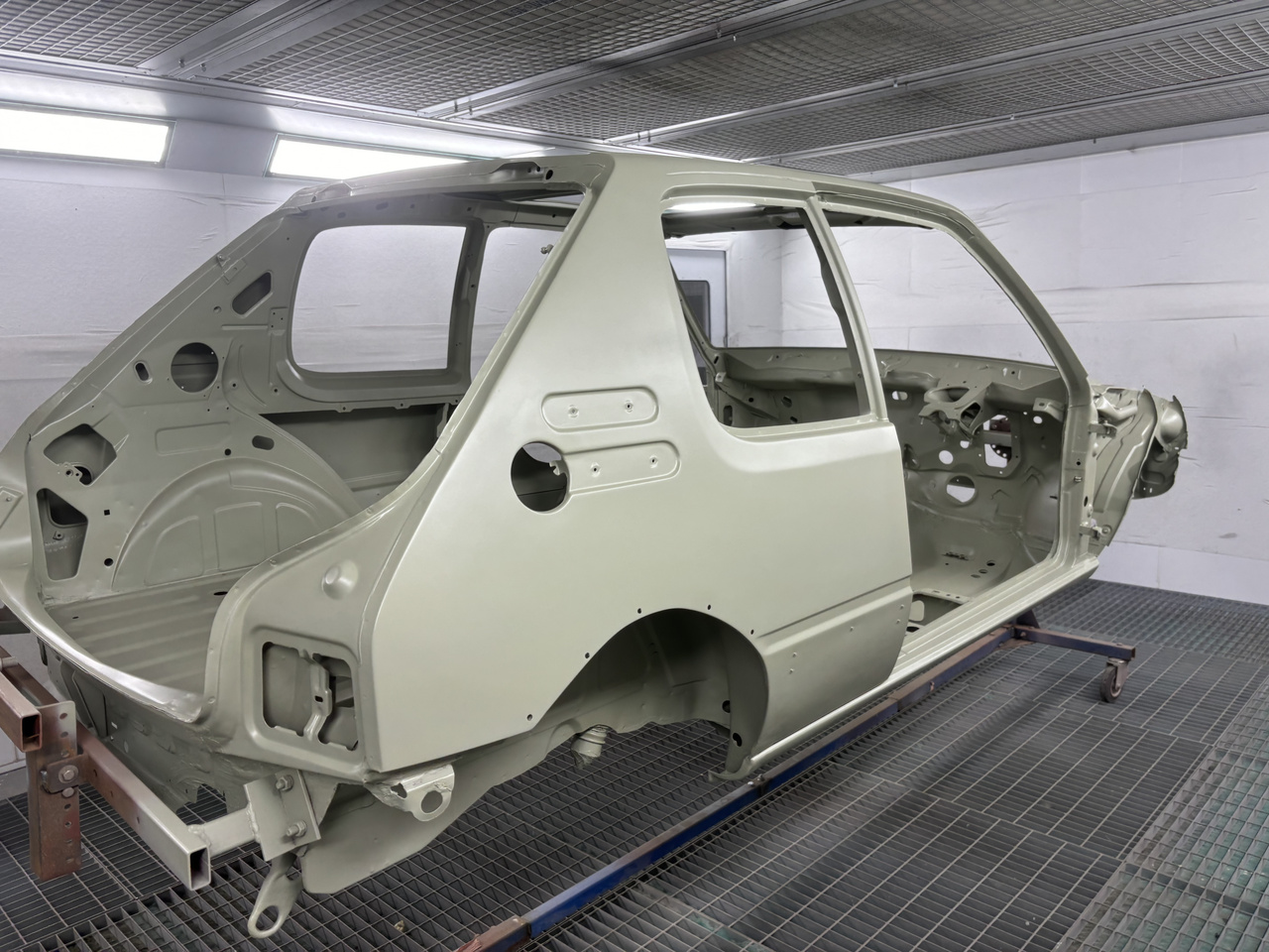 Peugeot 205 GTI shell undergoing full restoration in a paint booth